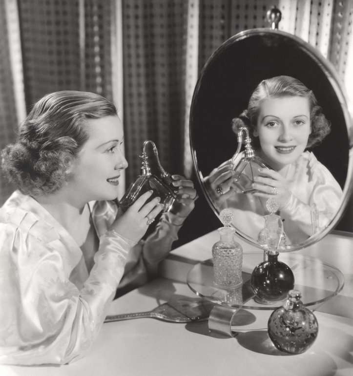 Reflection of woman holding perfume atomizer in mirror